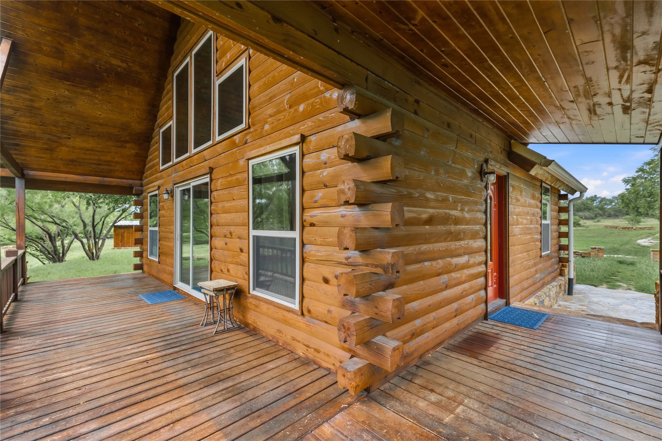 Log cabin exterior featuring a covered porch, multiple windows, a red entry door, and a sliding glass door