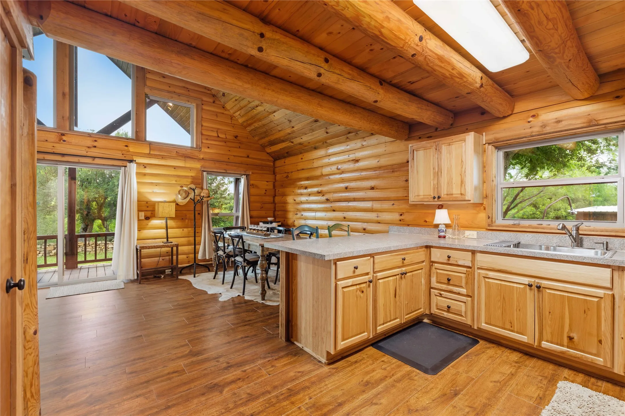 Open-concept kitchen and dining area featuring wood-finish flooring, natural wood log walls, and exposed ceiling beams