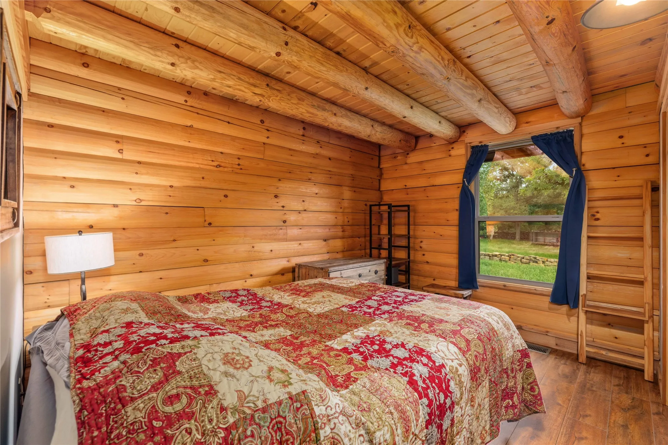 Log cabin interior featuring natural wood walls and ceiling beams, wood-finish flooring, and a window with exterior visibility