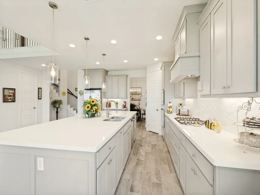 Spacious kitchen featuring a large island with an undermount sink, pendant lighting, white countertops, light gray cabinetry, and wood-look tile flooring