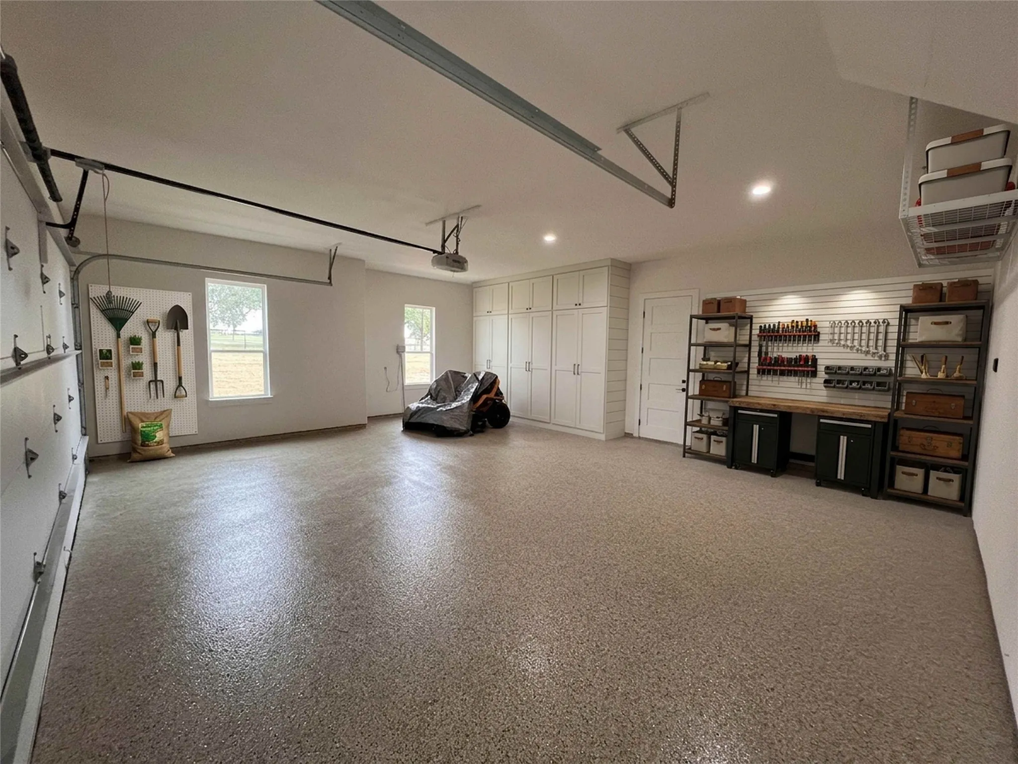 Spacious garage featuring a durable epoxy floor coating, recessed lighting, and ample built-in storage cabinetry
