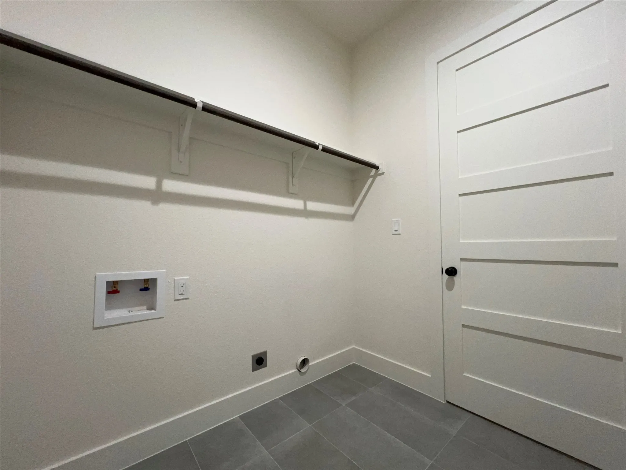 Laundry area featuring a hanging rod, modern panel door with black hardware, and gray tile flooring
