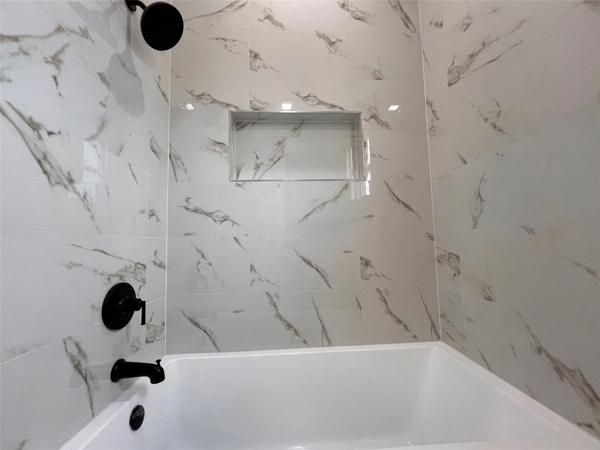 Bathtub with matte black fixtures, white tile surround with gray veining, and a recessed shower niche