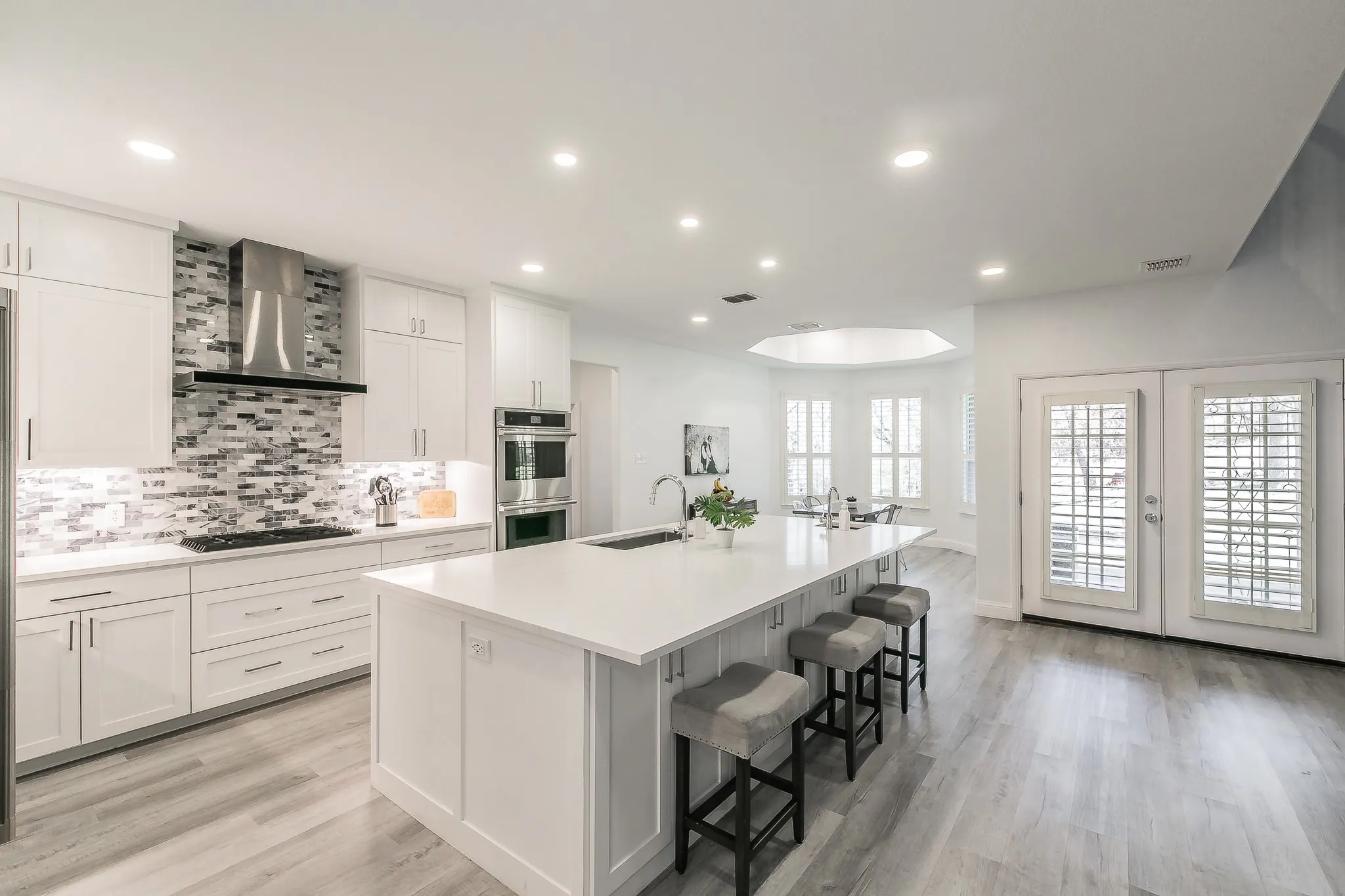 Kitchen featuring double oven, an island with sink, stovetop, wall chimney exhaust hood, and a sink