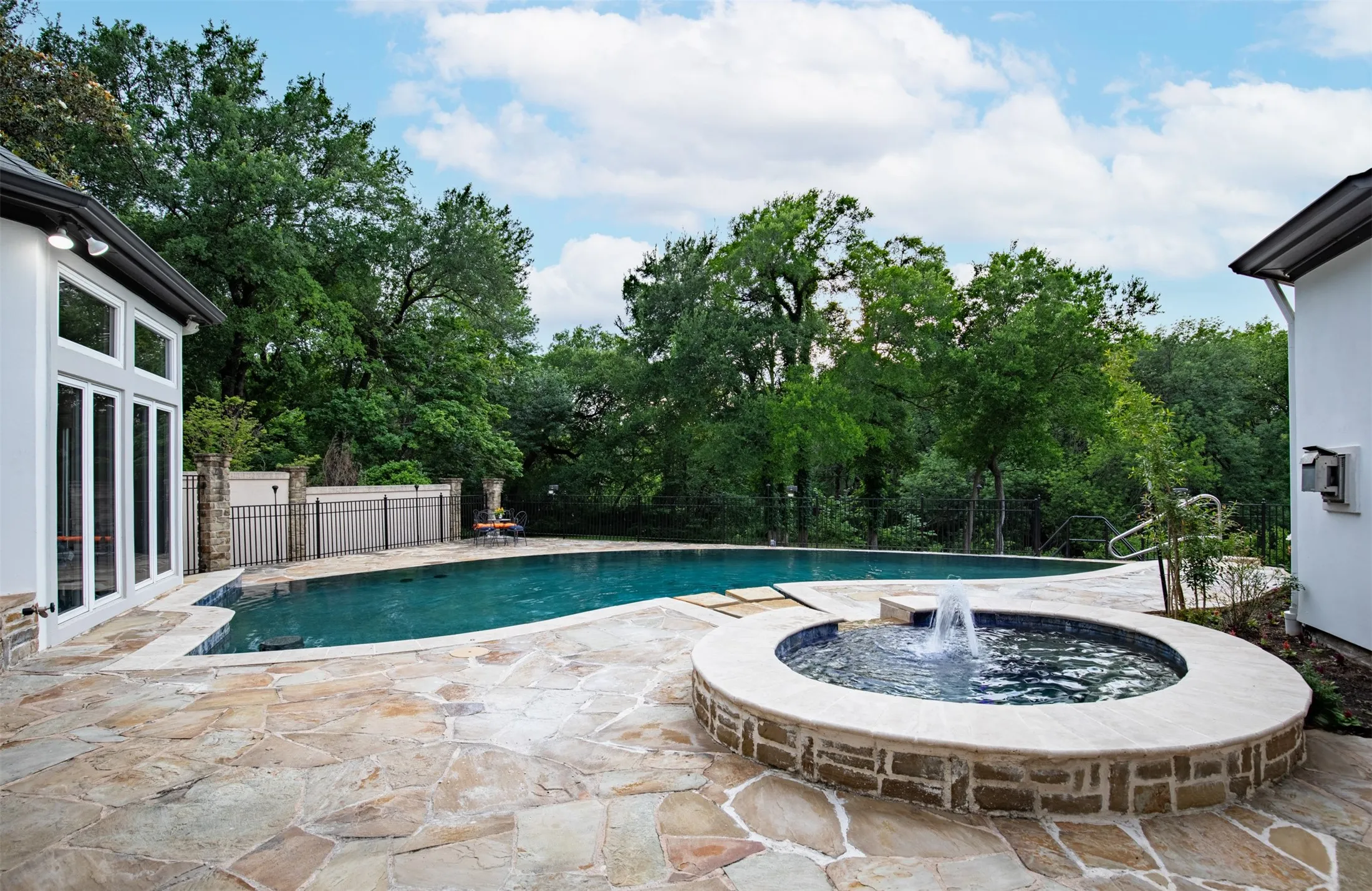 Expansive flagstone patio featuring a dark-bottom swimming pool and an integrated circular spa with water feature