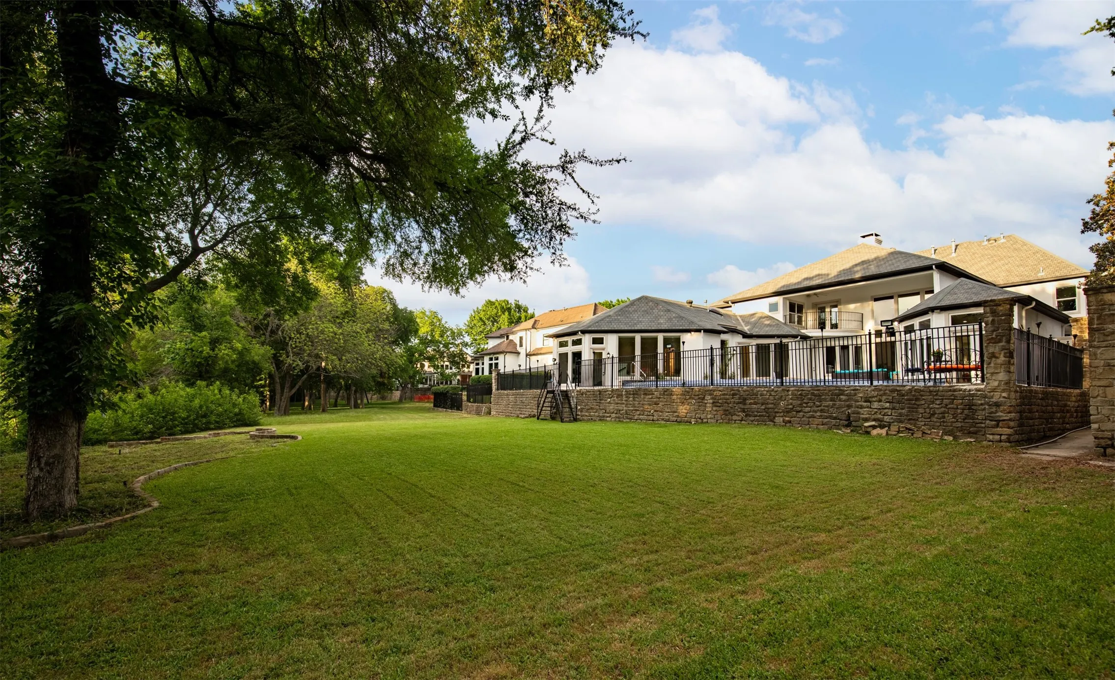 Expansive green lawn with mature trees and stone retaining wall