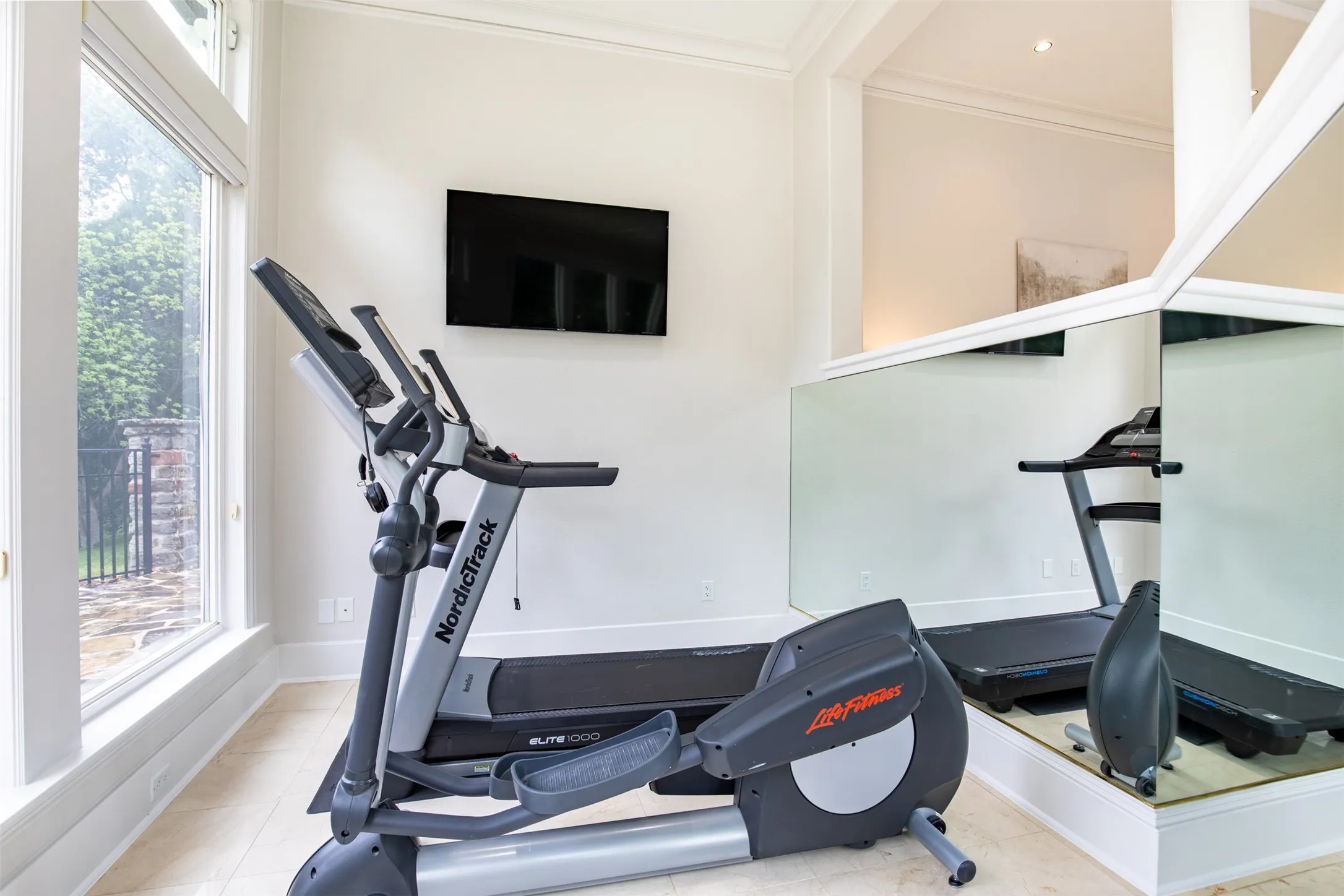 Dedicated exercise space featuring large windows, crown molding, a wall-mounted display, and mirrored walls