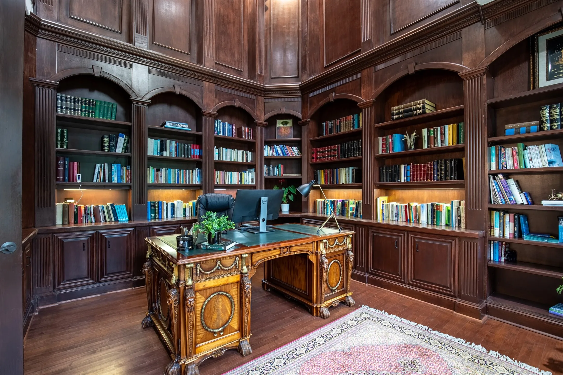 Wood-paneled study featuring extensive built-in shelving, integrated cabinetry, arched alcoves, and wood-finish flooring