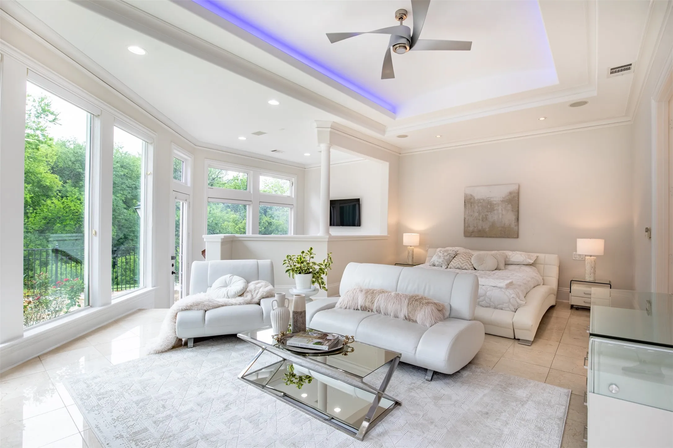 Spacious primary retreat with tiered ceiling, stylish fan, travertine flooring, and lower level seating area perfect from office or exercise space