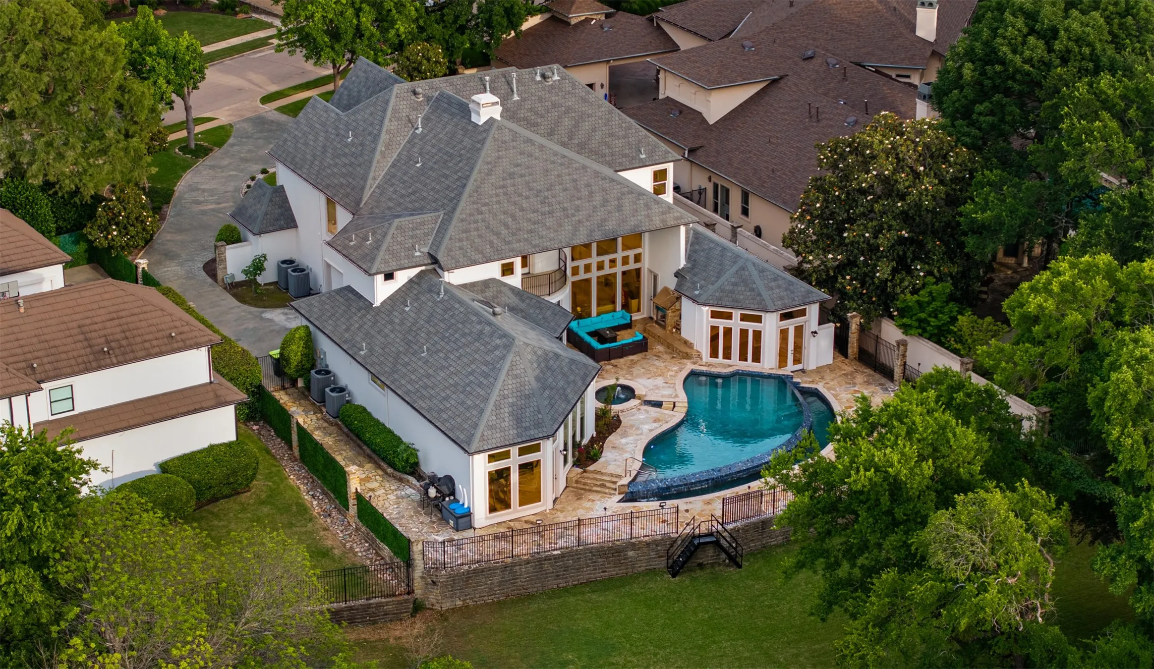 Expansive property featuring a multi-level white stucco exterior, grey shingle roofing, and a patterned driveway