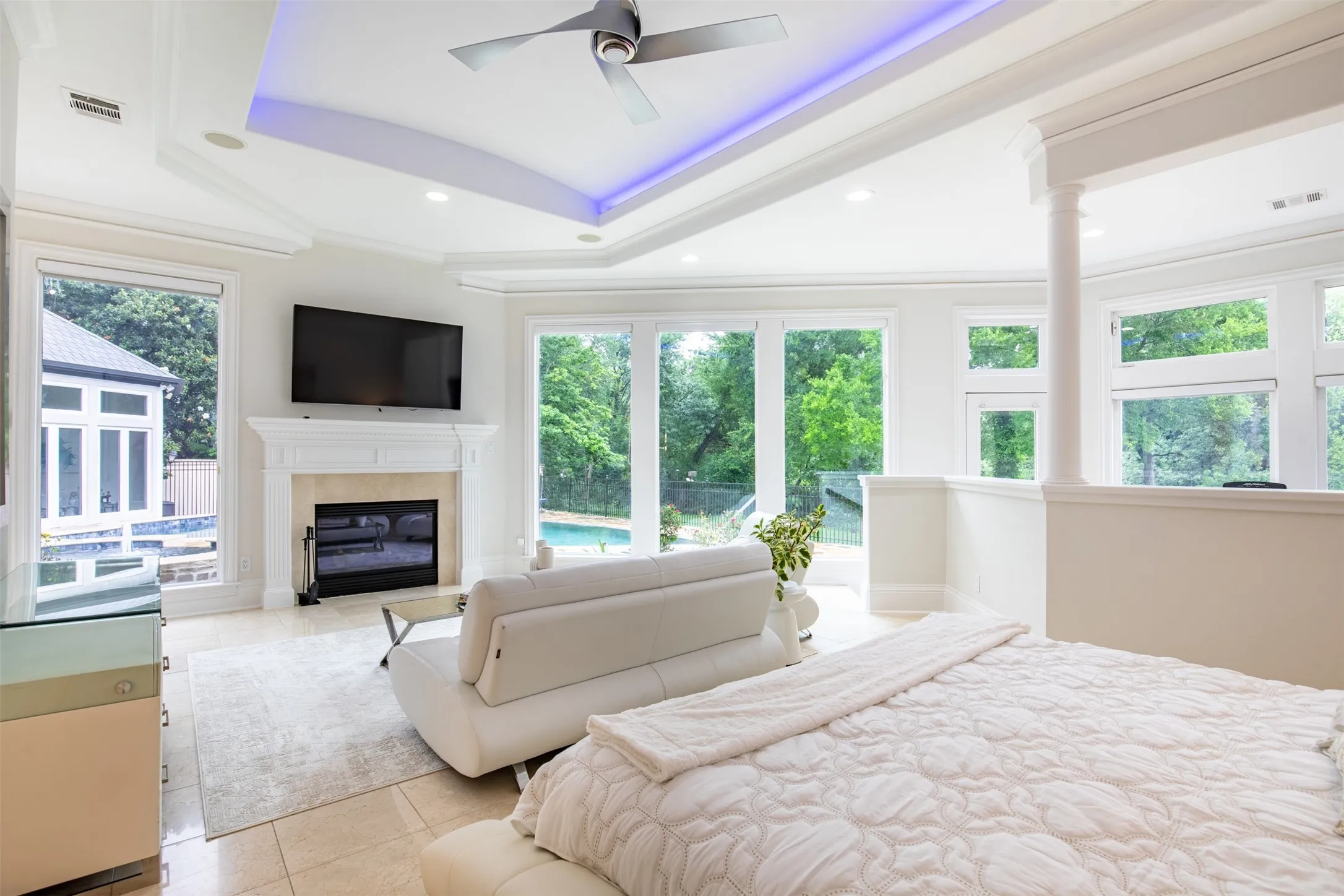 Spacious room featuring tile flooring, a fireplace with a white mantel, and extensive windows showcasing outdoor greenery
