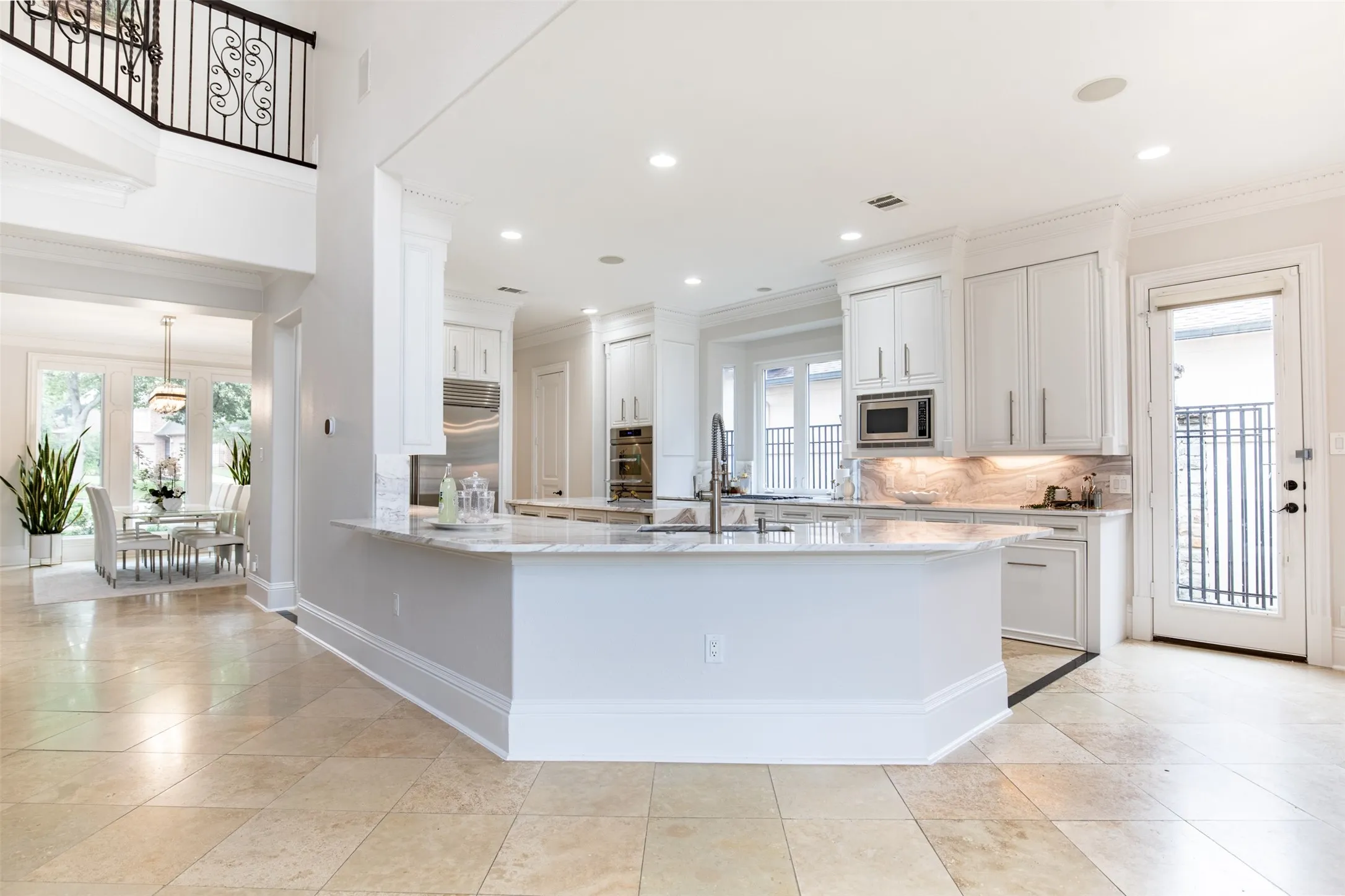 Gourmet kitchen featuring a large central island with an undermount sink, stainless steel appliances, white cabinetry, recessed lighting, and light-toned tile flooring