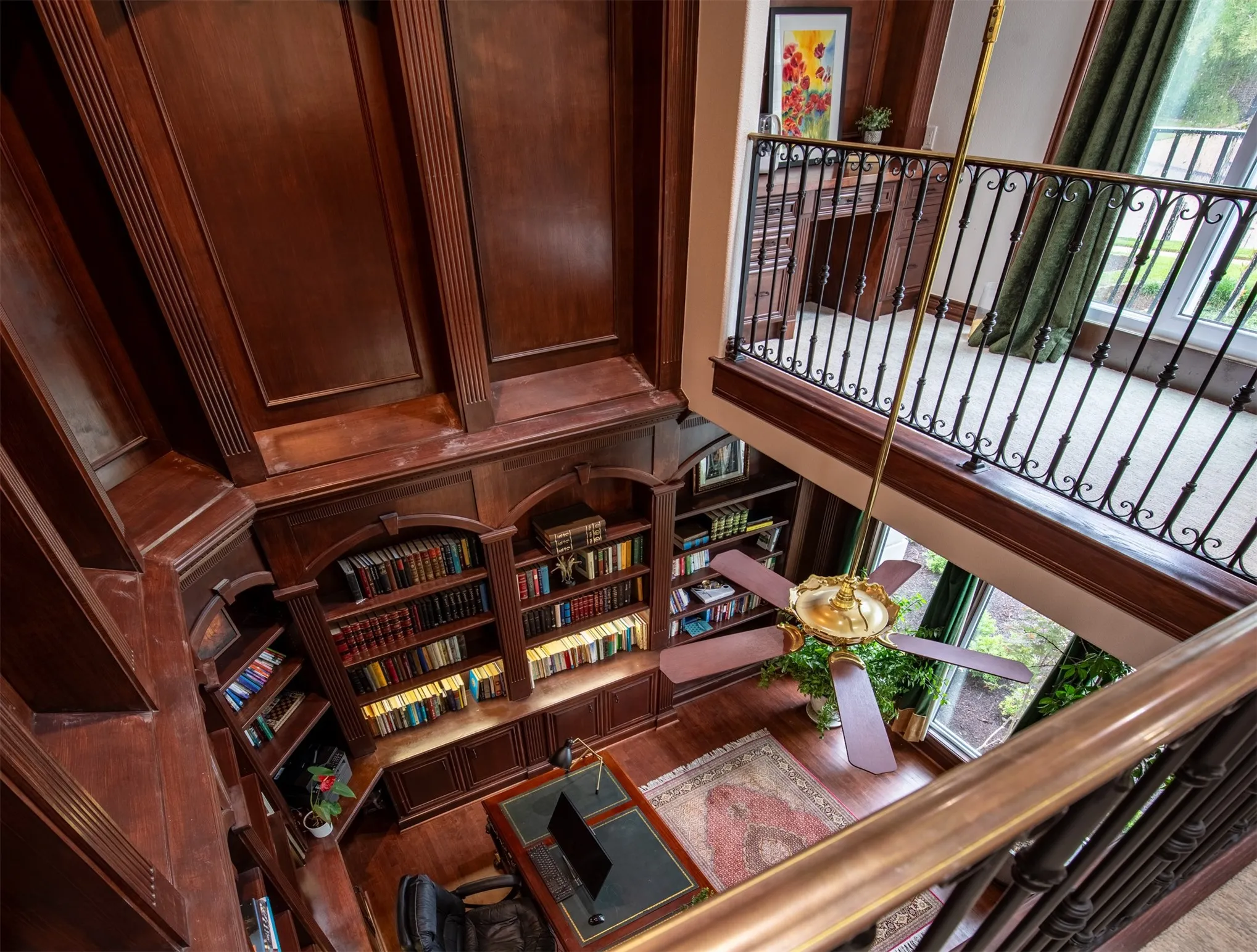 Two-story study featuring extensive wood paneling, built-in bookshelves with integrated lighting, wood-finish flooring, and a decorative ceiling fan
