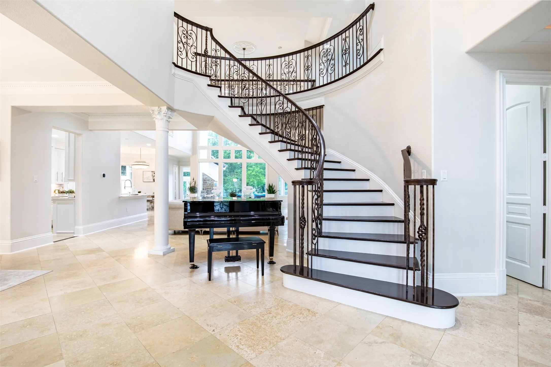 Grand two-story foyer featuring a curved staircase with wrought iron balusters and dark wood treads, light stone tile flooring, a decorative ceiling medallion, and a white architectural column