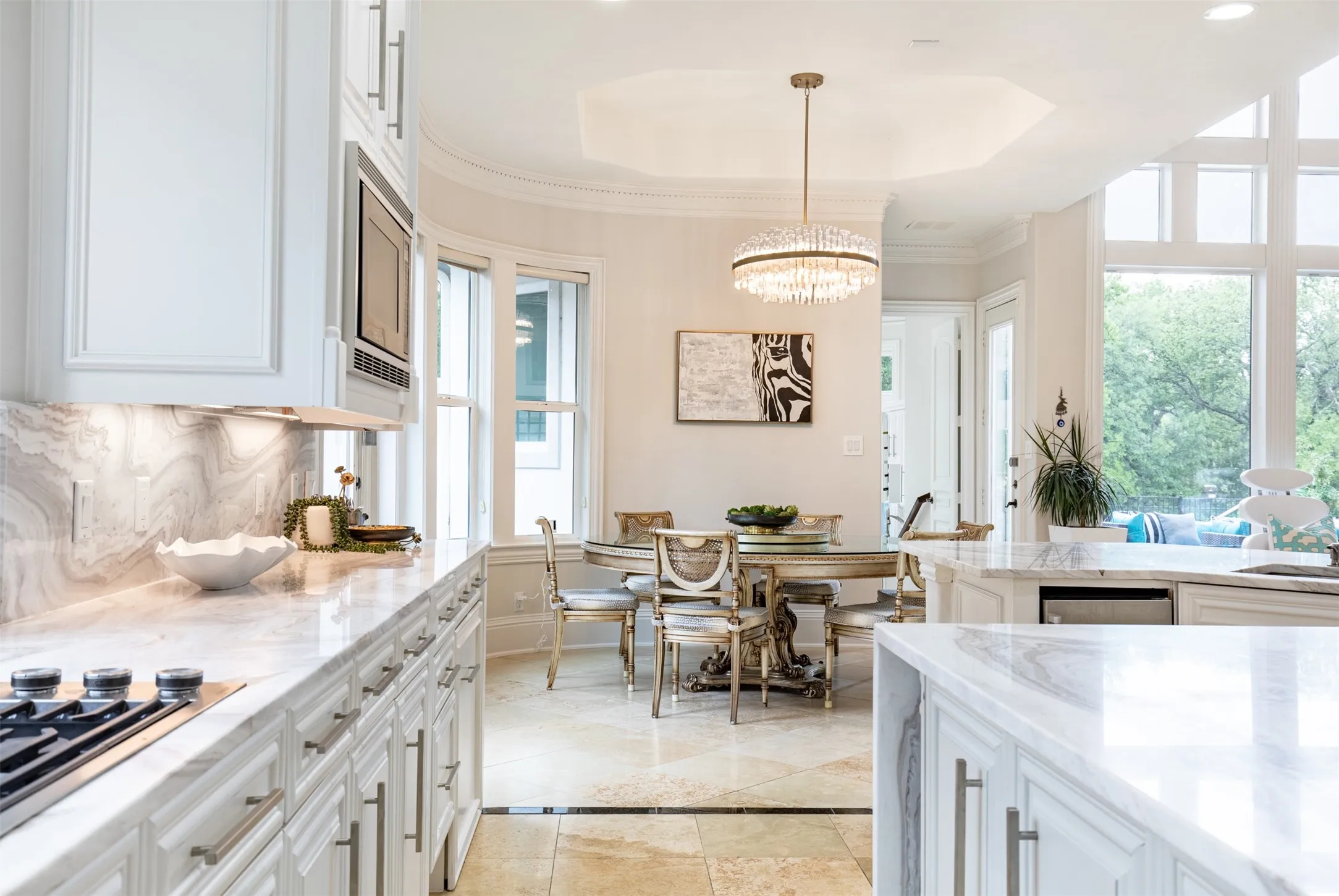 Gourmet kitchen and dining area featuring a gas cooktop, integrated microwave, white cabinetry with brushed nickel hardware, and marble countertops with a matching backsplash