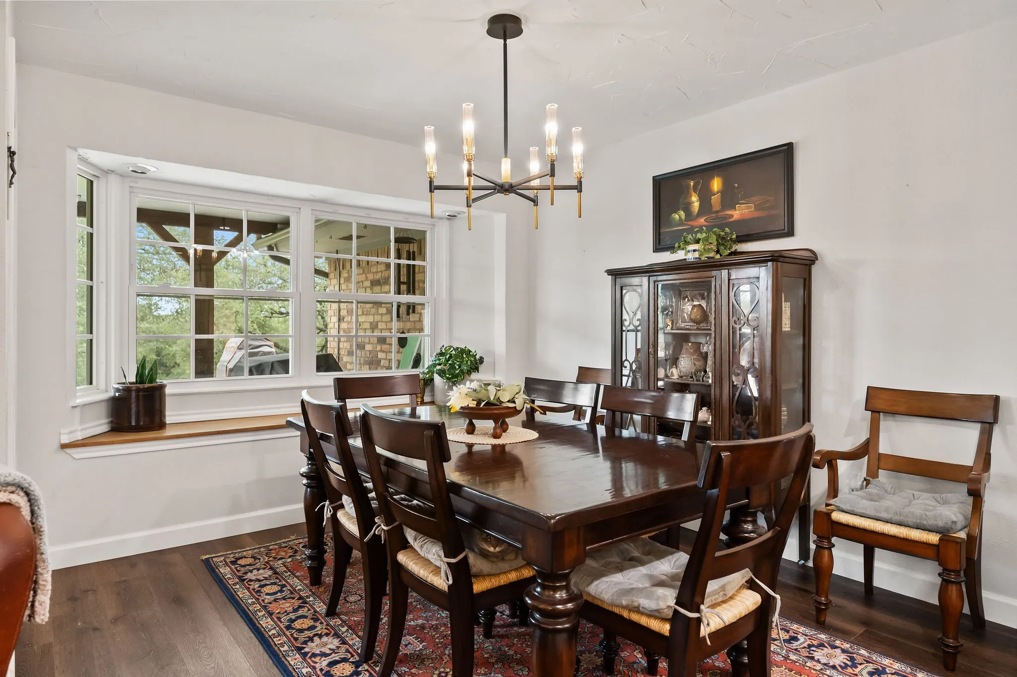 Dining space featuring a bay window with a wood sill, dark wood-finish flooring, a modern chandelier with gold and black accents, and white wall finishes