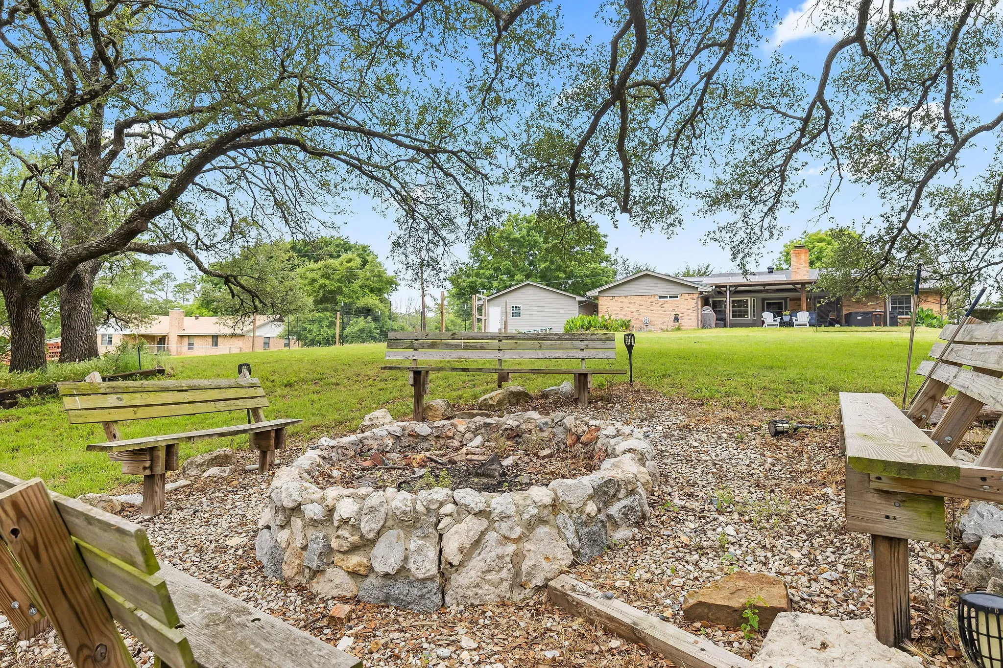 Outdoor fire pit area featuring a stone-lined fire pit, surrounding wooden benches, and a gravel base