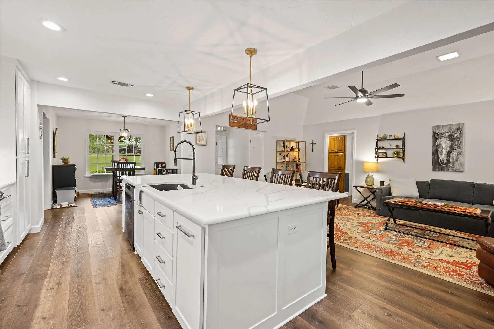 Kitchen island with white cabinetry, a large sink, and a high-arc faucet, complemented by wood-finish flooring