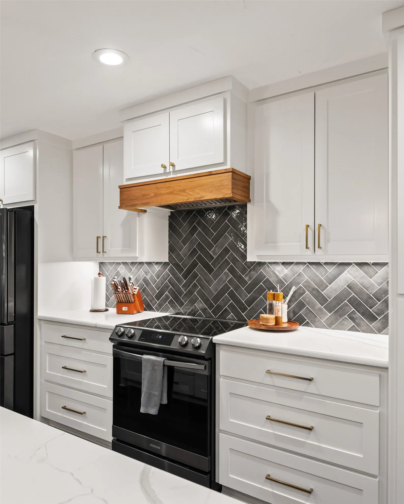 Kitchen featuring a herringbone tile backsplash, white shaker-style cabinetry, a built-in range with a wood-finish range hood, recessed lighting, and quartz countertops