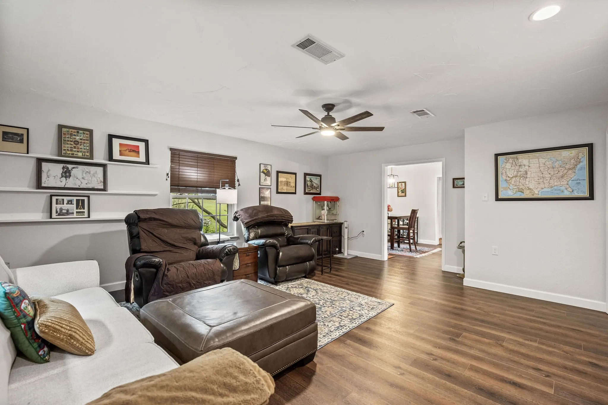 Spacious living area featuring wood-finish flooring, a ceiling fan, recessed lighting, and wall-mounted shelving