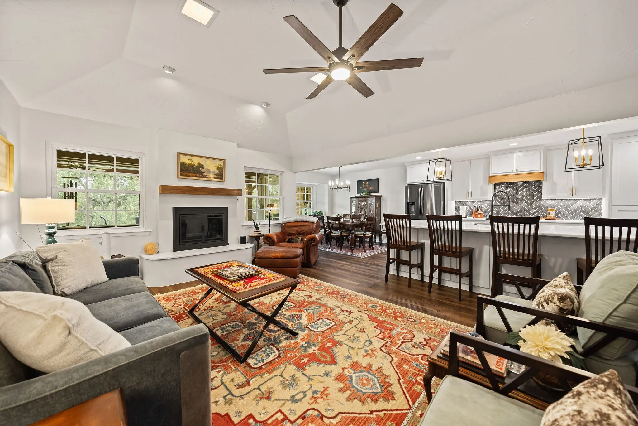Open-concept living area featuring vaulted ceilings, wood-finish flooring, a fireplace with a wood mantle, and a kitchen island with seating