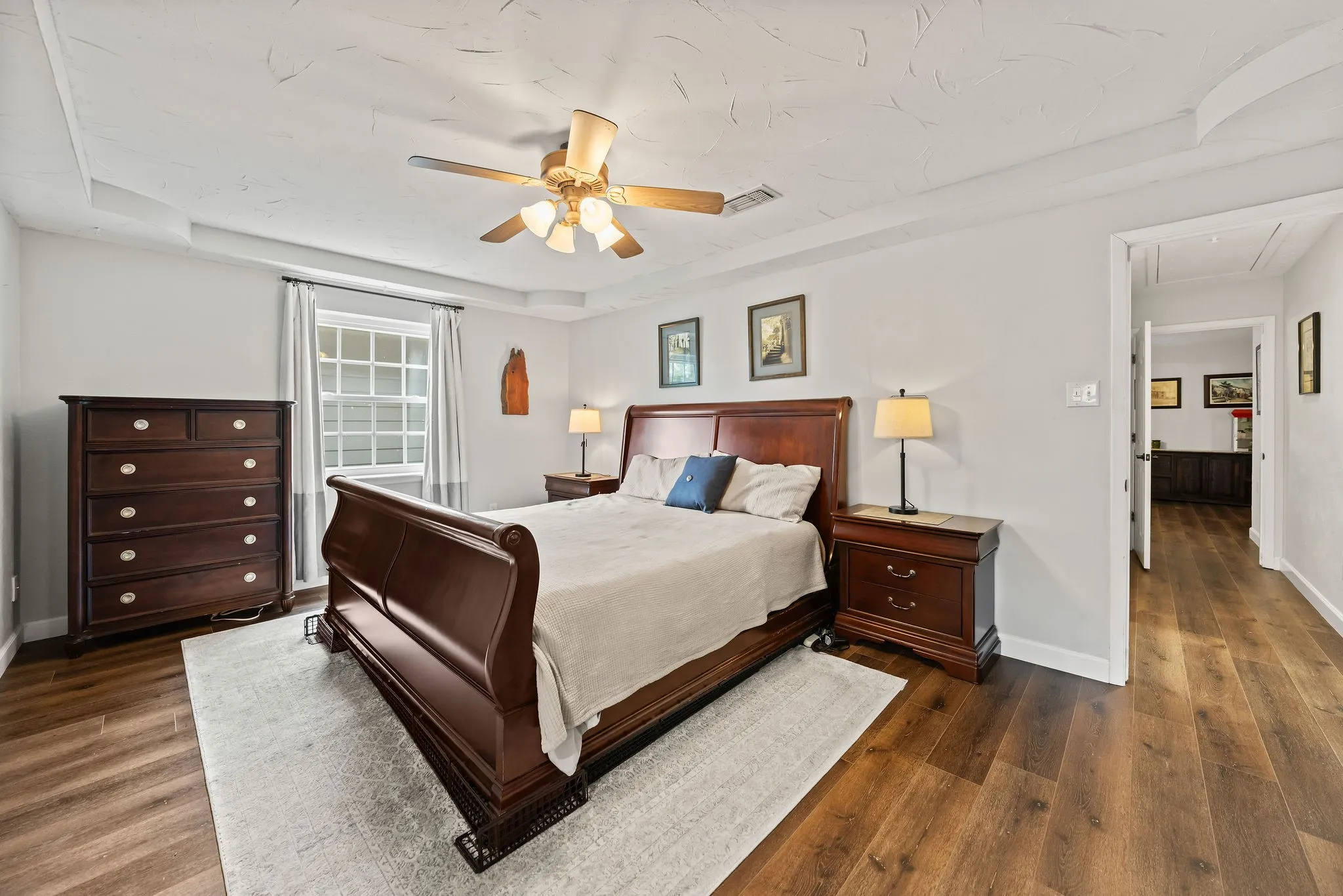 Spacious room featuring wood-finish flooring, a tray ceiling, and a ceiling fan with integrated lighting
