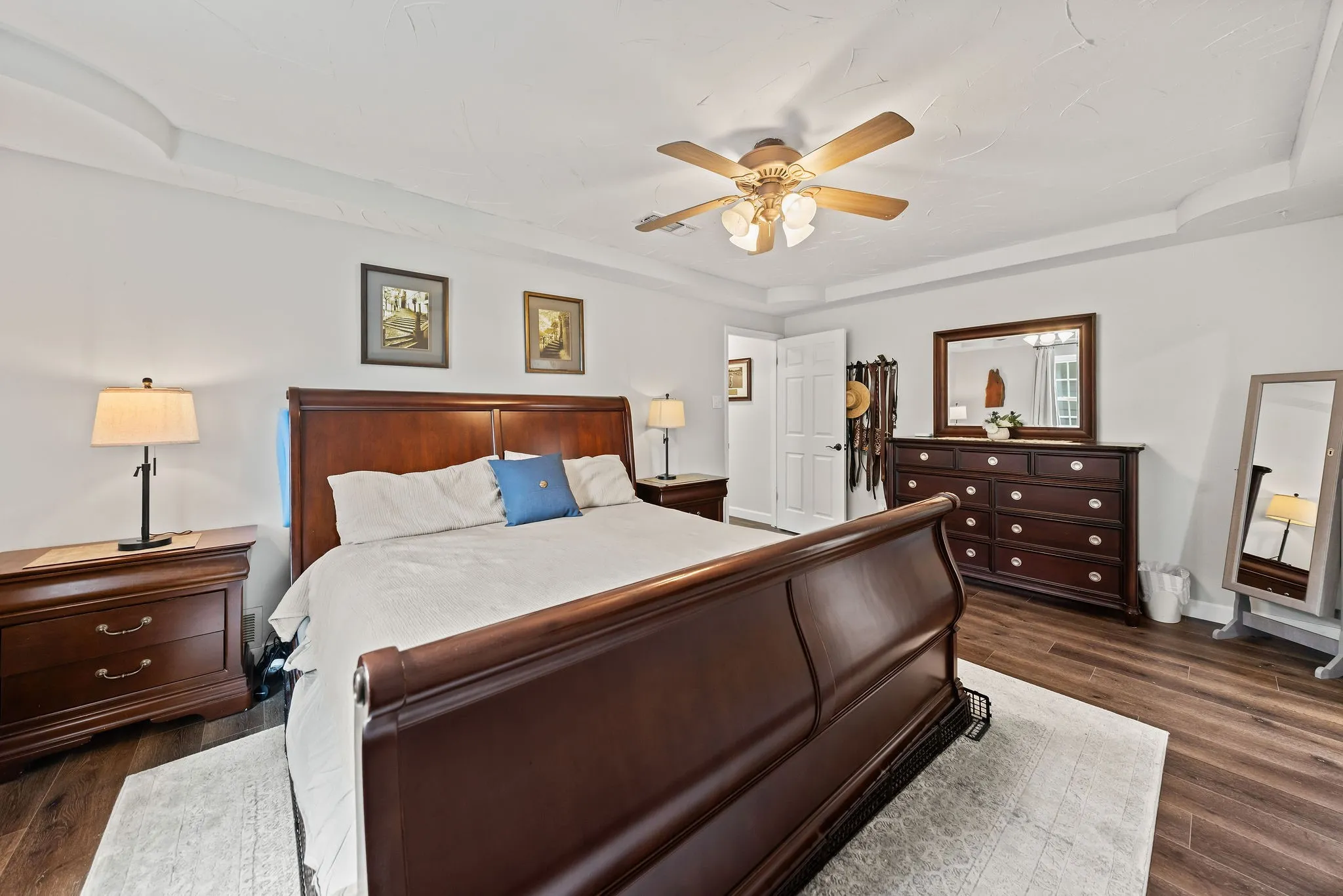 Spacious bedroom featuring a tray ceiling, ceiling fan, wood-finish flooring, and white walls