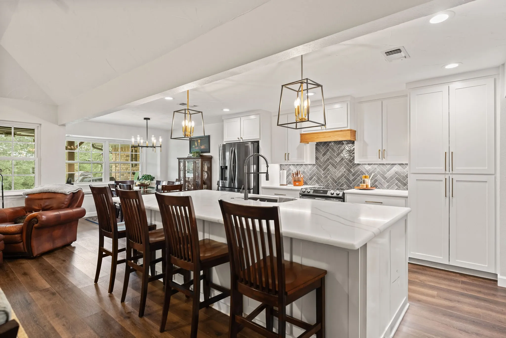 Open-concept kitchen with a large island, white shaker cabinetry, stainless steel appliances, and herringbone tile backsplash