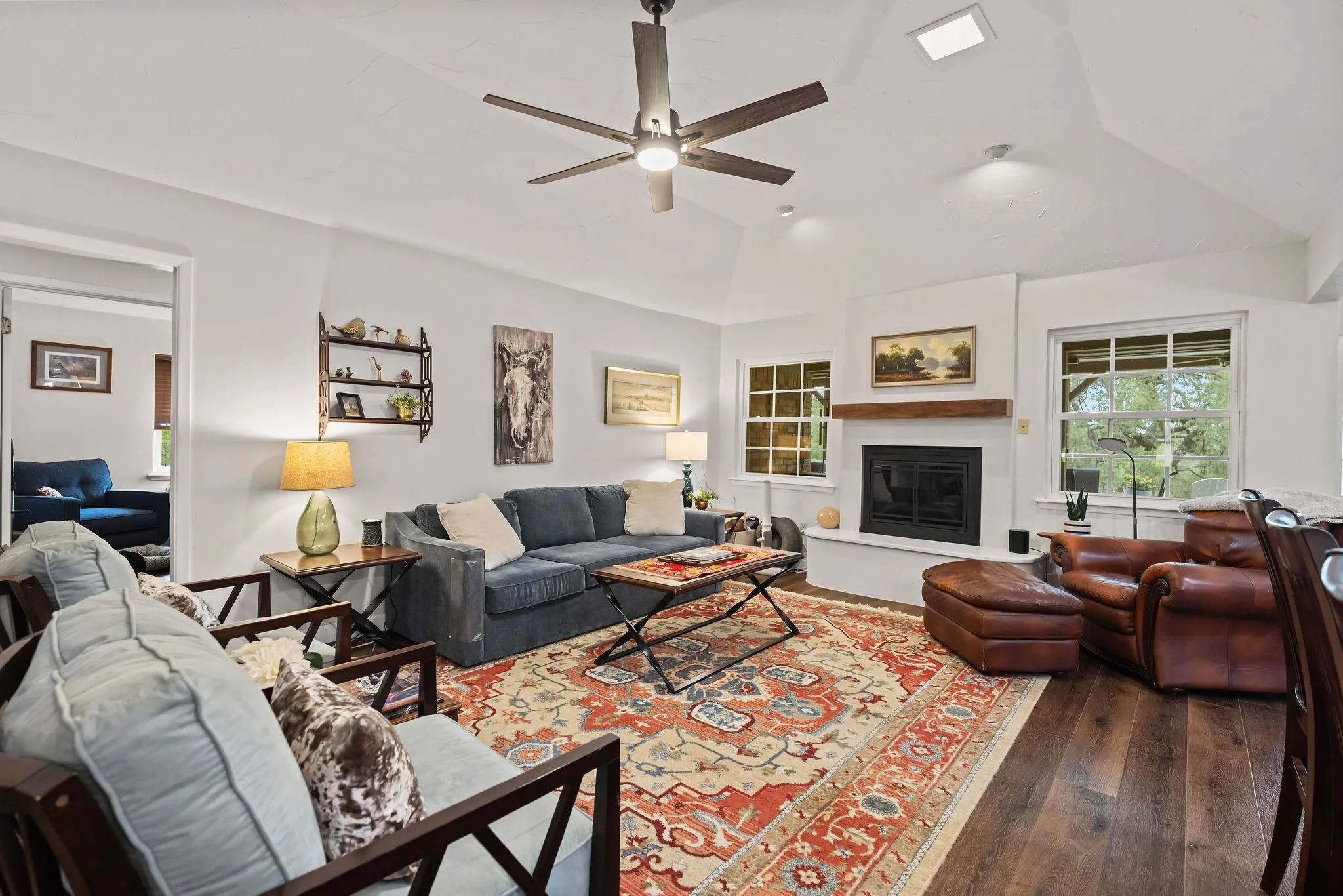 Spacious living area featuring vaulted ceilings, wood-finish flooring, a fireplace with a wood mantle, and multiple windows