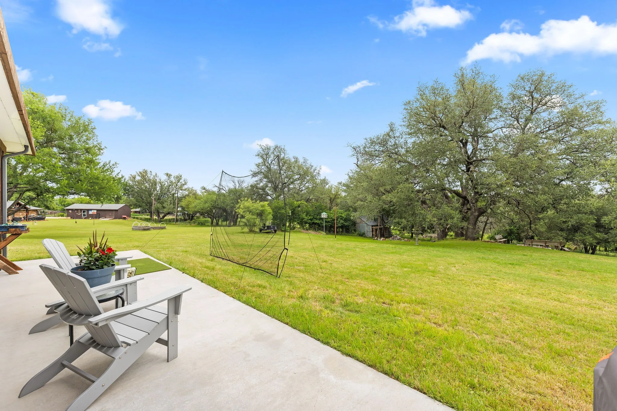 Expansive green lawn with mature trees and a concrete patio