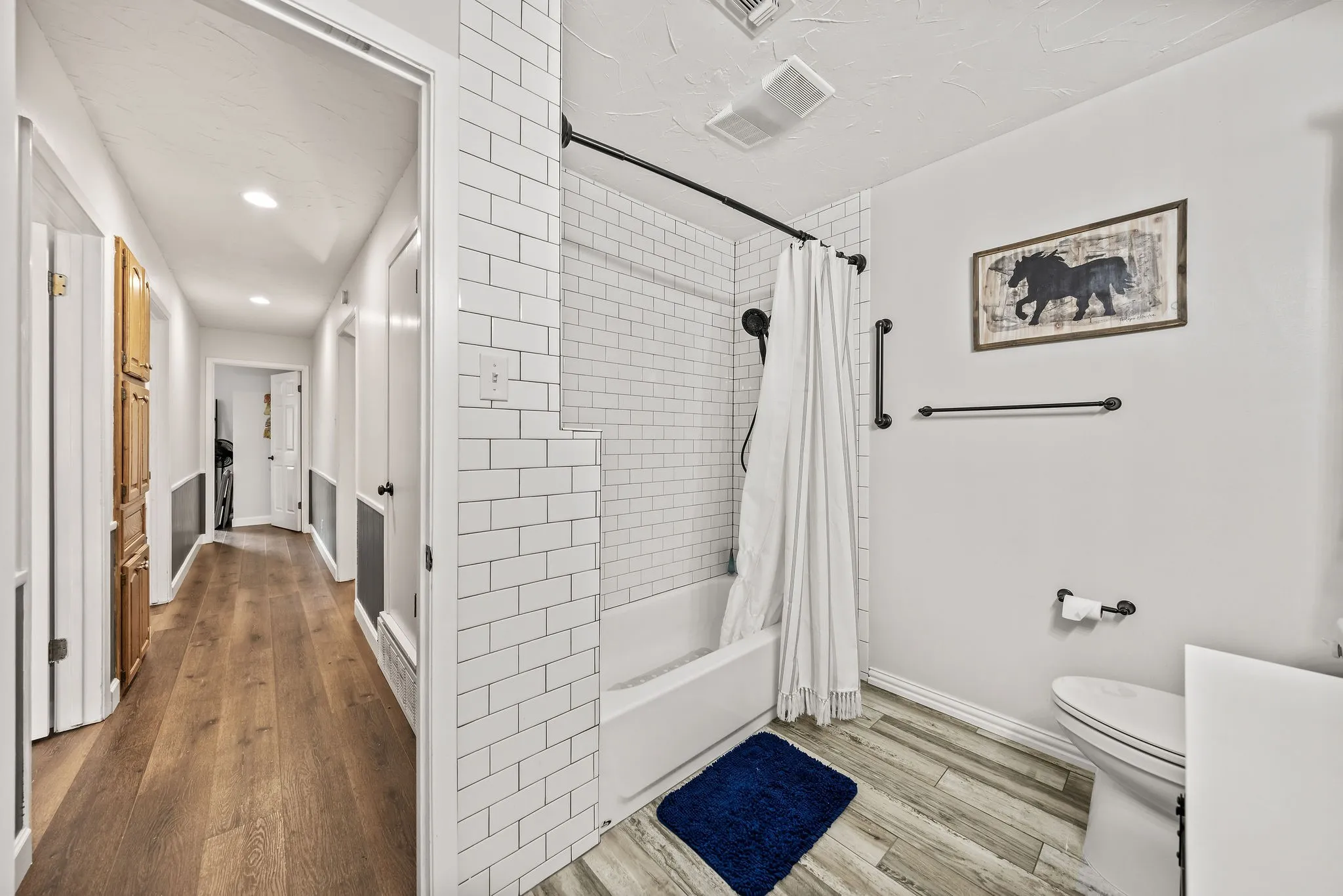 Full bathroom featuring a white subway tile tub surround, dark-finish fixtures, and wood-finish flooring