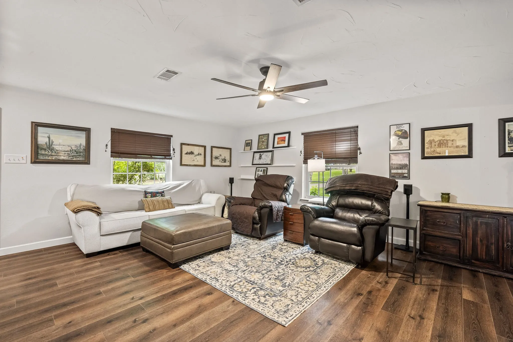 Spacious living area featuring wood-finish flooring, light-toned walls, and a ceiling fan with integrated lighting