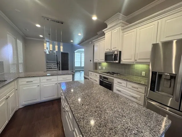Expansive kitchen featuring a large island with stone countertops, white cabinetry with crown molding, stainless steel appliances, and wood-finish flooring