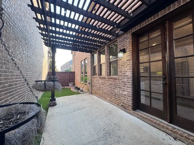 Brick exterior featuring a concrete patio, dark wood pergola, and French doors