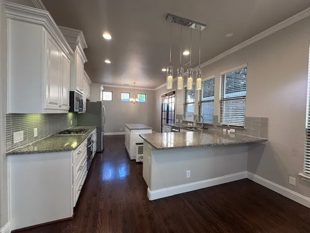 Modern kitchen featuring white cabinetry, granite countertops, a tile backsplash, wood-finish flooring, and a central island with pendant lighting