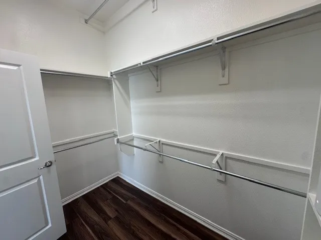 Walk-in closet featuring wood-finish flooring, white walls, and multiple clothing rods with shelving
