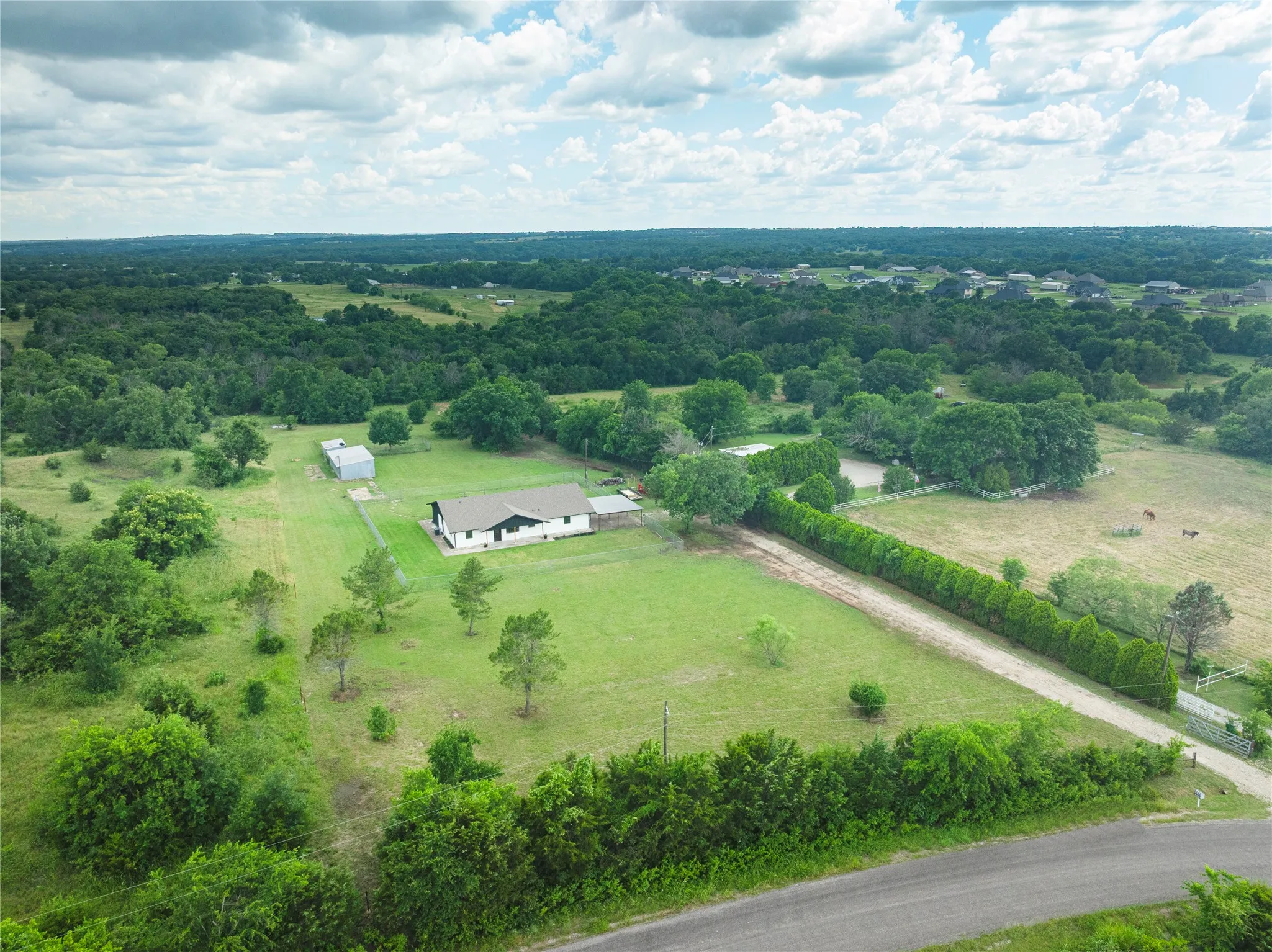 Expansive property featuring a single-story residence, detached outbuilding, mature trees, and a gravel driveway