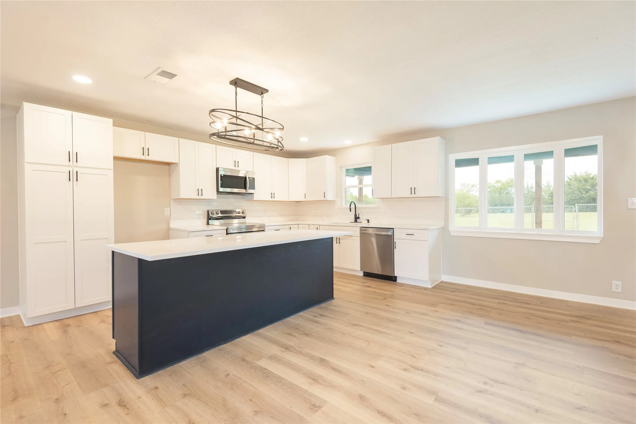 Modern kitchen featuring an expansive island with a contrasting dark base, white shaker cabinetry, stainless steel appliances, and wood-finish flooring