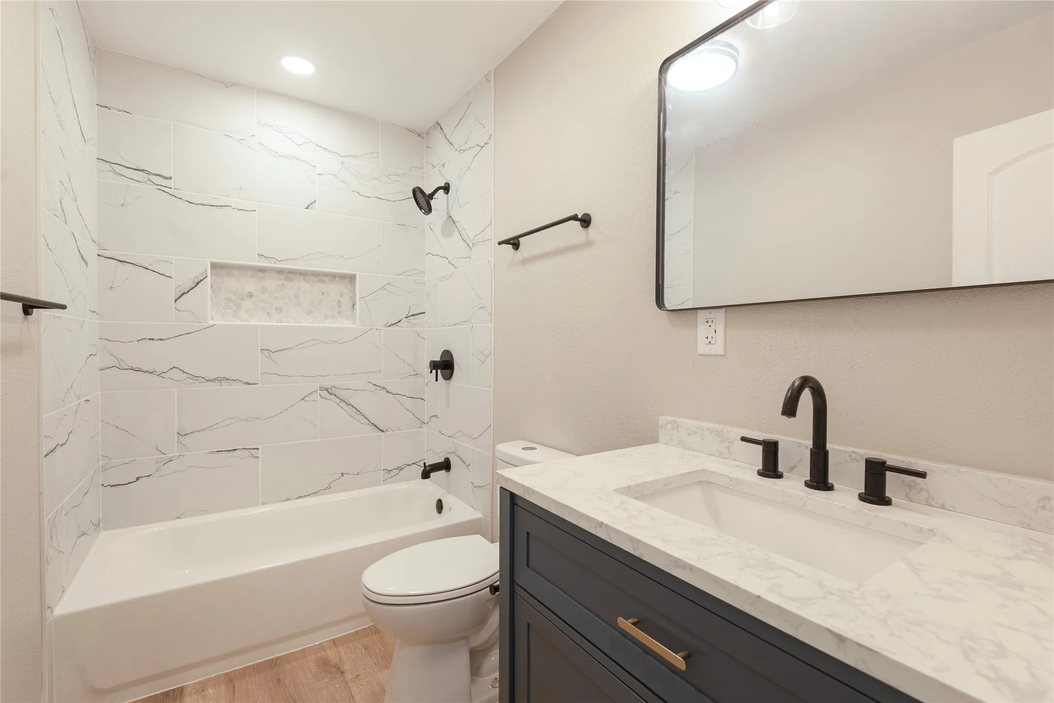 Bathroom featuring a white bathtub with a tile surround, a built-in shower niche, a dark blue vanity with a light-colored countertop, and matte black fixtures