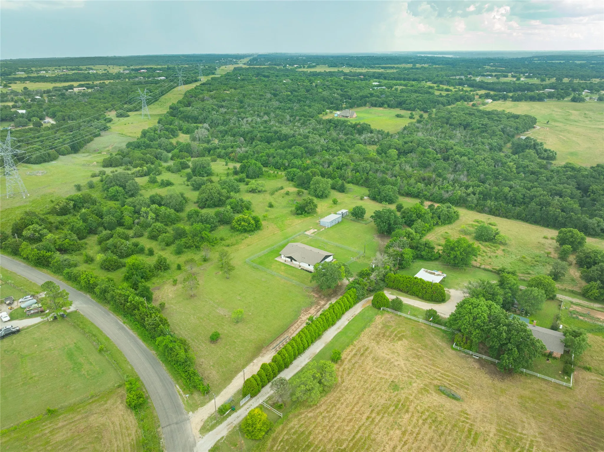Expansive property featuring a residence with a light-colored roof, multiple outbuildings, and a tree-lined driveway