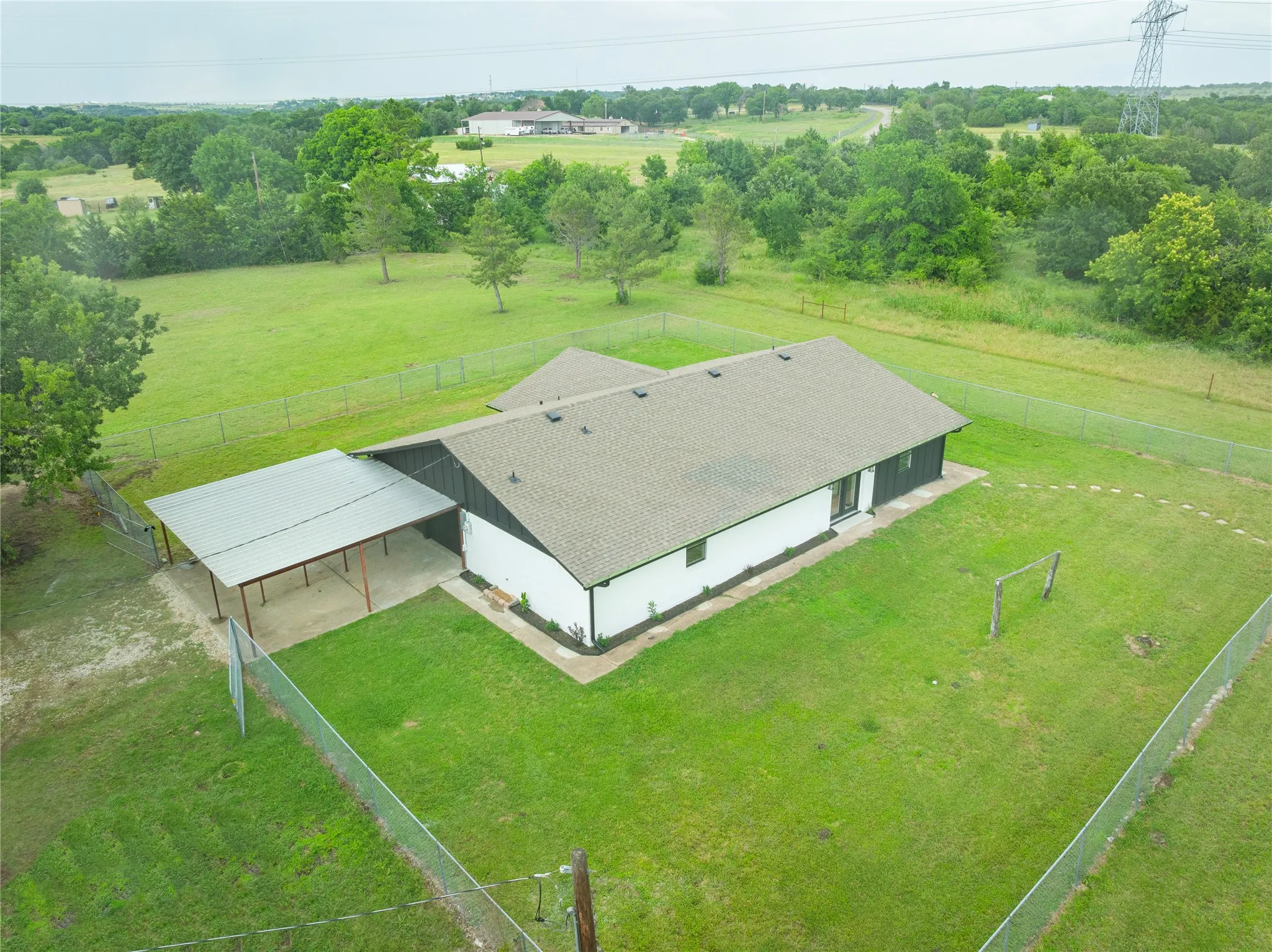 Expansive fenced property featuring a single-story residence with a gray shingle roof, white and dark gray exterior siding, and a covered carport with a metal roof