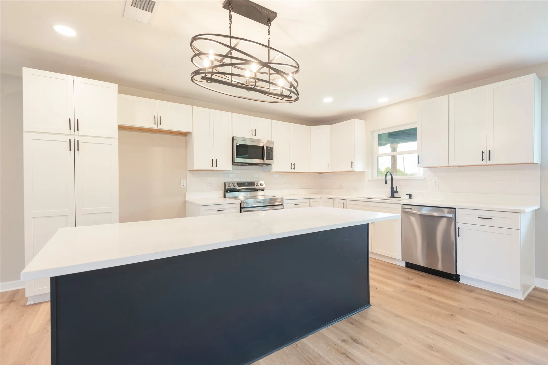 Kitchen featuring an expansive island with a white countertop, white shaker cabinetry, stainless steel appliances, and wood-finish flooring
