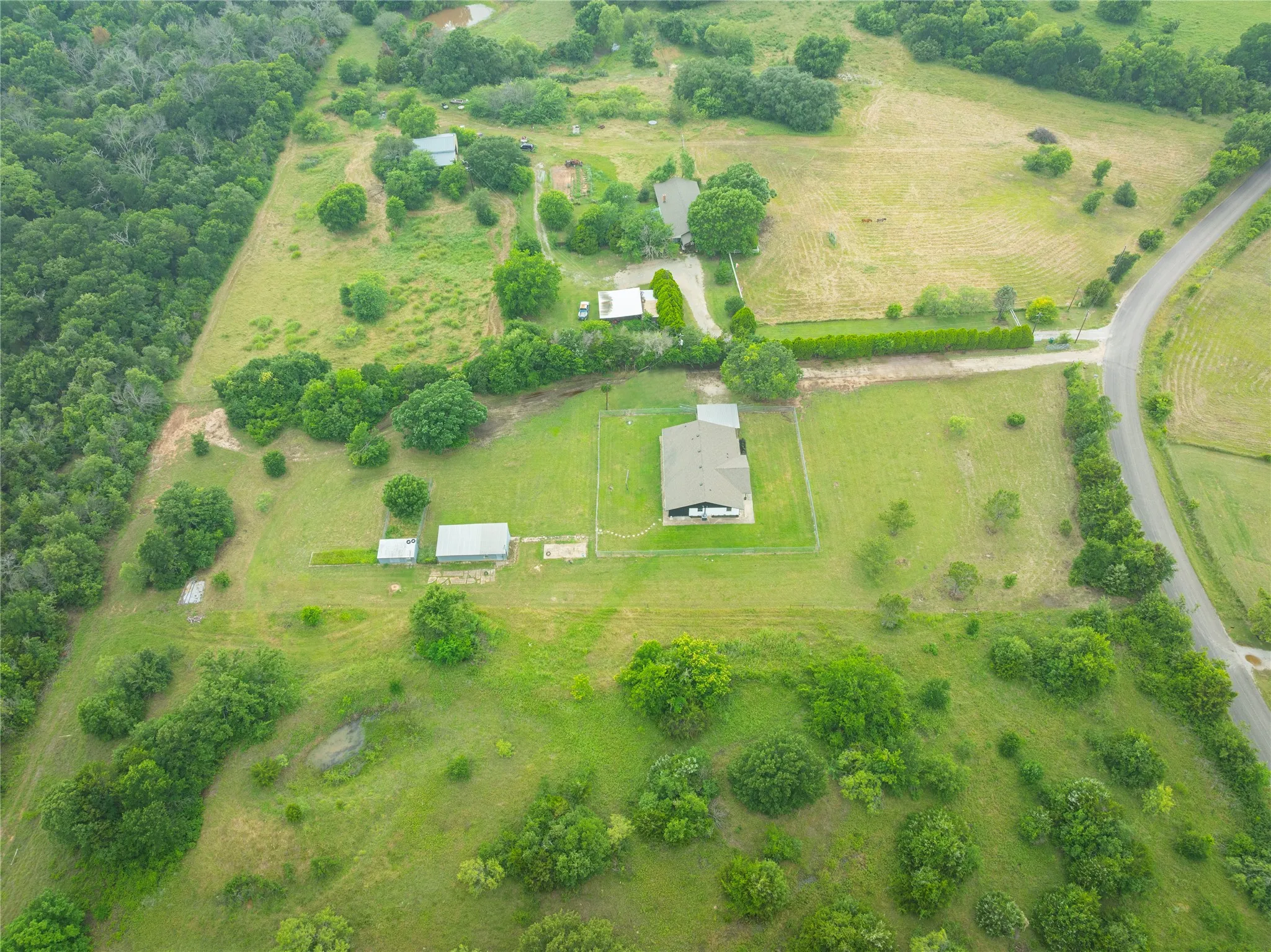 Expansive rural property featuring a primary residence with a dark roof, multiple outbuildings, and a tree-lined perimeter