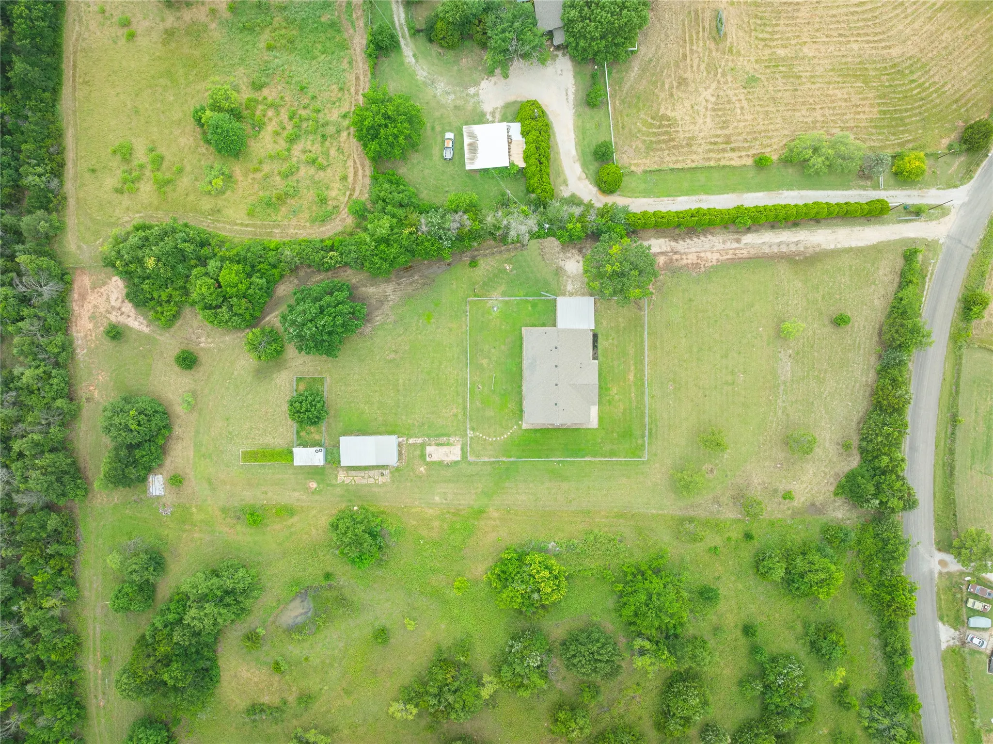 Expansive green acreage featuring a primary residence with a fenced perimeter, a secondary building with an adjacent covered area, and a tertiary building