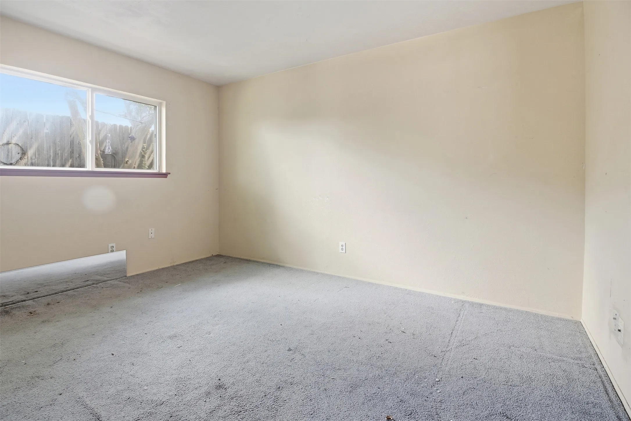 Room with light-colored walls and a window featuring a purple-hued sill