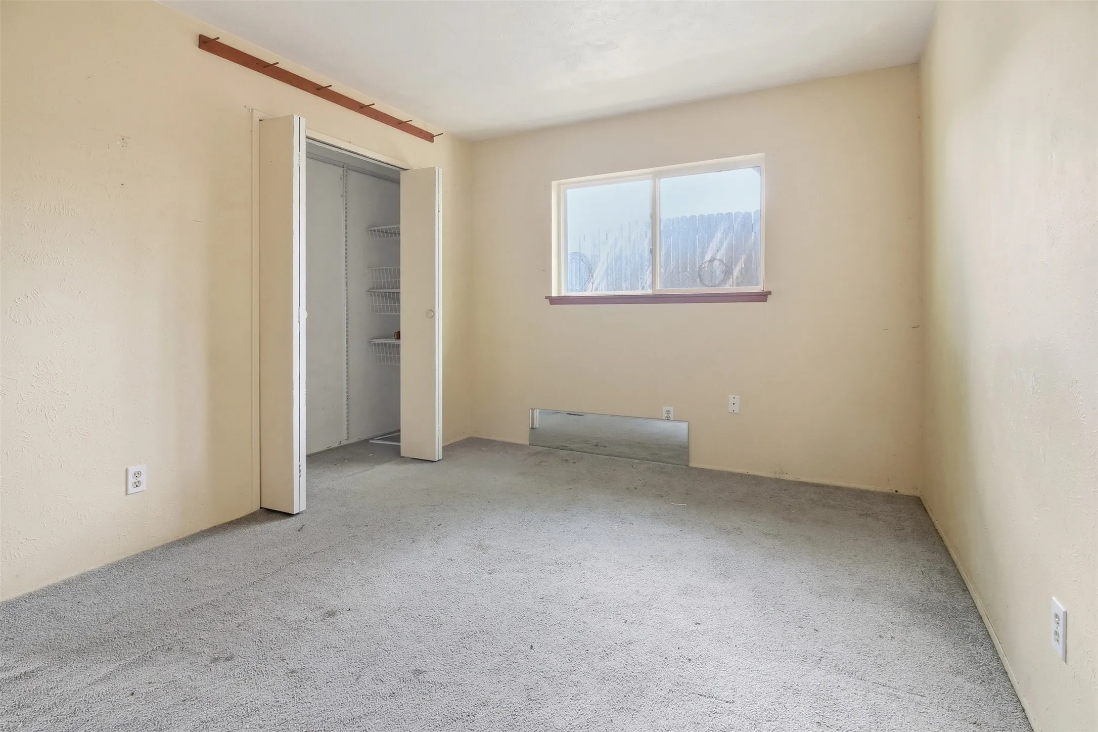 Carpeted room featuring light-toned walls, a window with a wood sill, and a bi-fold door closet with built-in shelving
