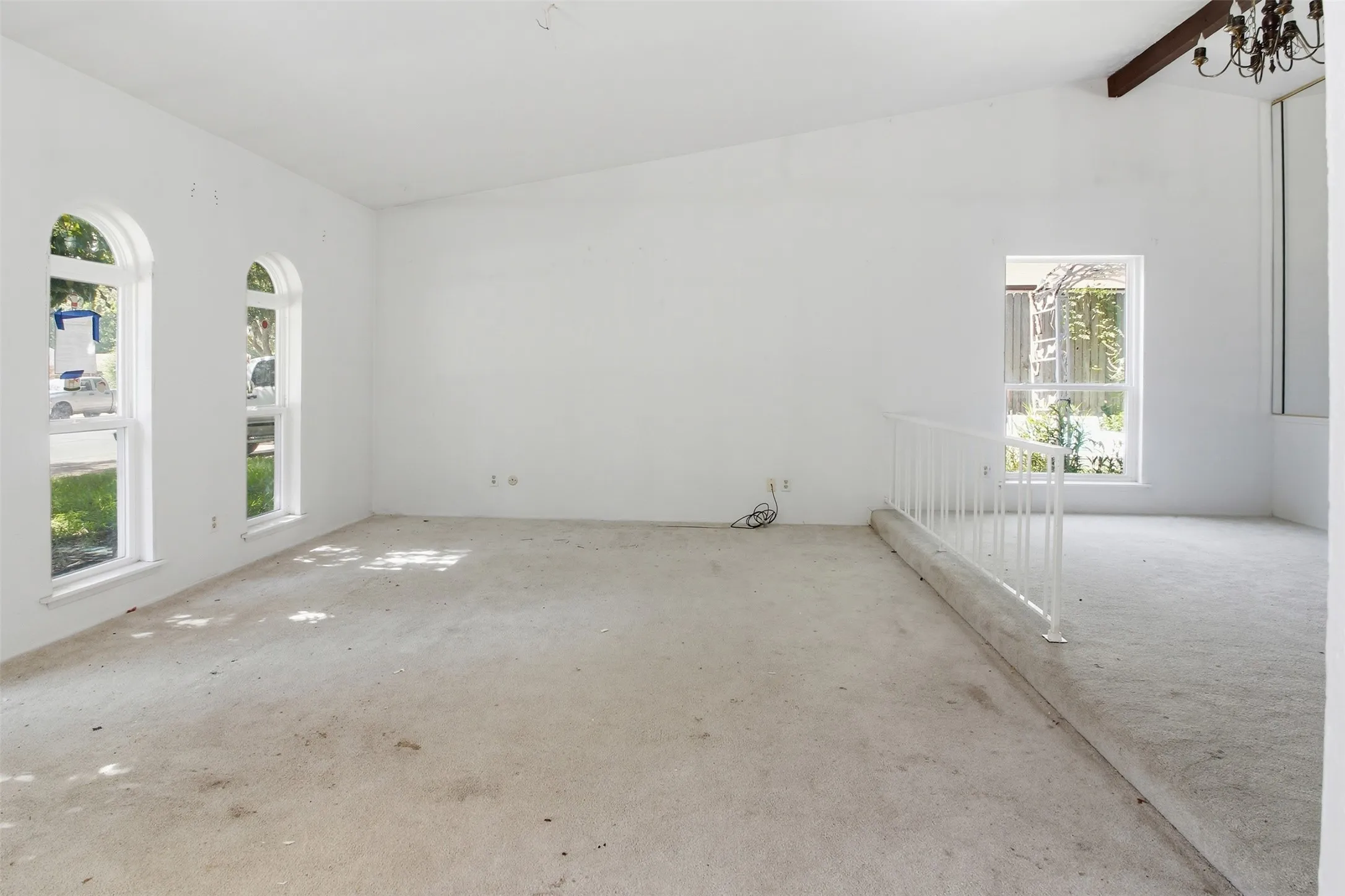 Spacious interior room featuring a vaulted ceiling with an exposed wood beam, arched windows, and a built-in railing