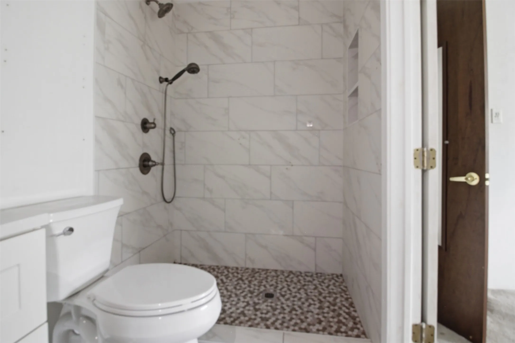Shower featuring white tile surround, pebble floor, and dual shower heads