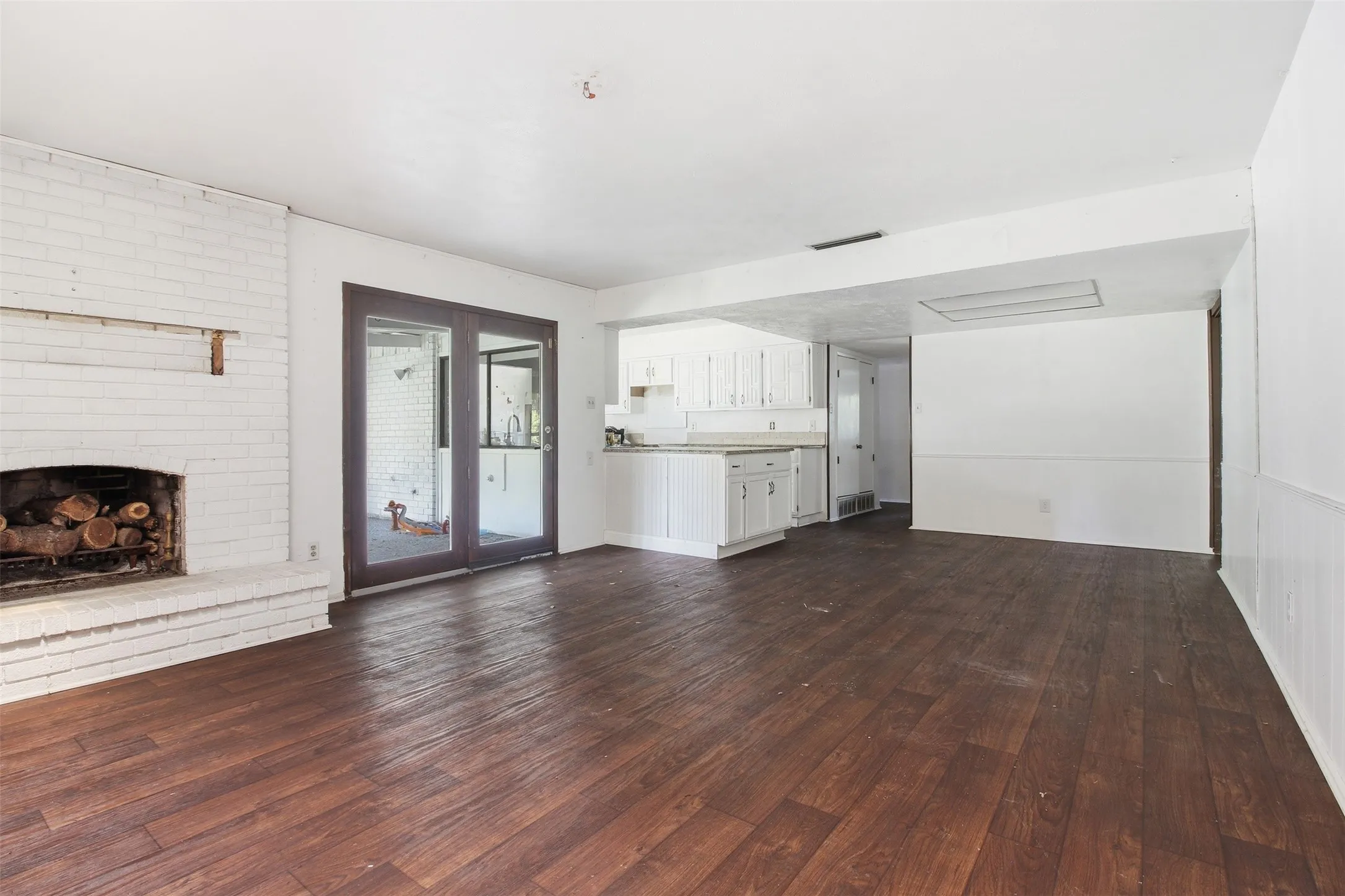 Expansive room featuring wood-finish flooring, a white-painted brick fireplace, and double glass doors