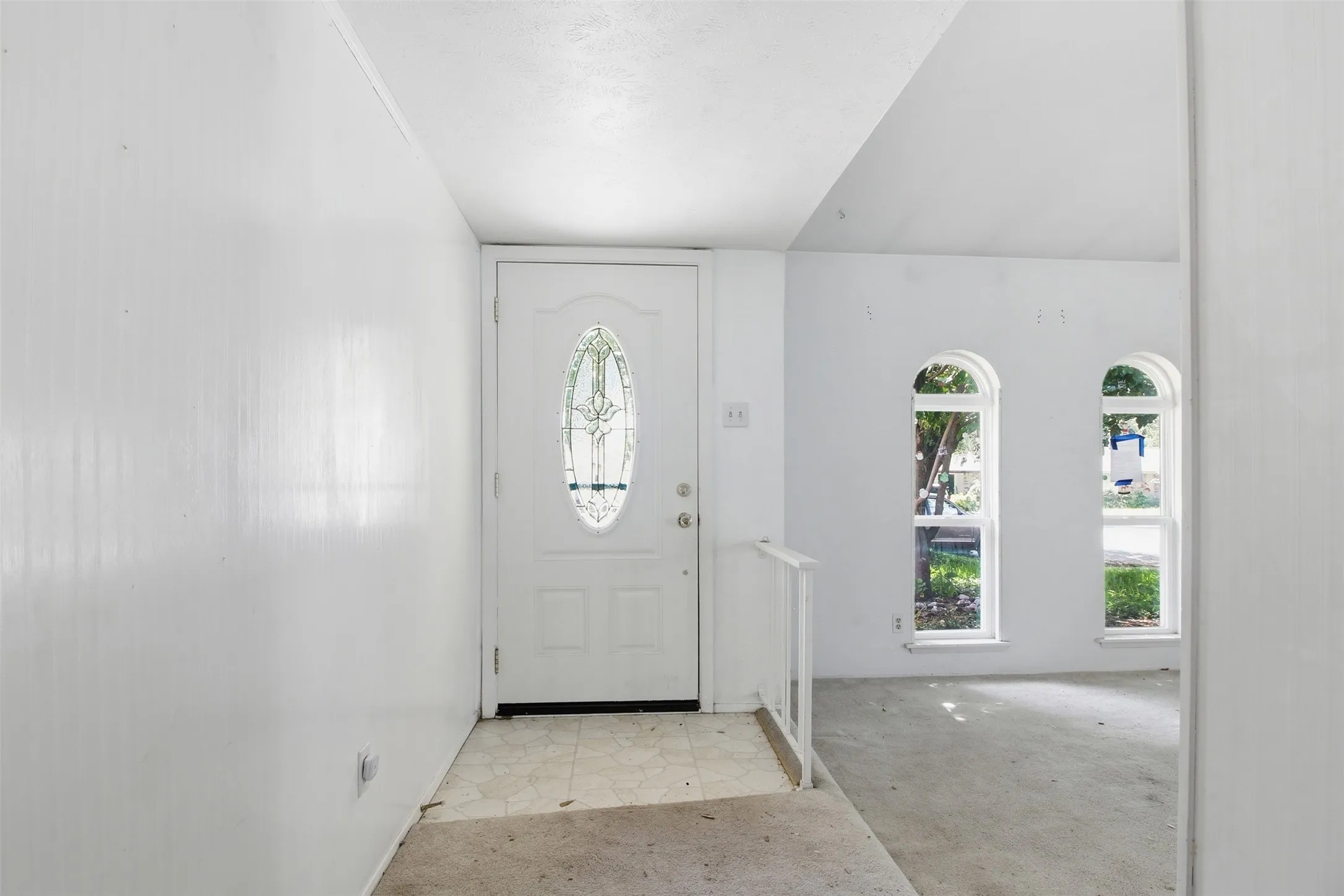 Entryway featuring a white door with an oval stained-glass insert, tile flooring, and a partial railing